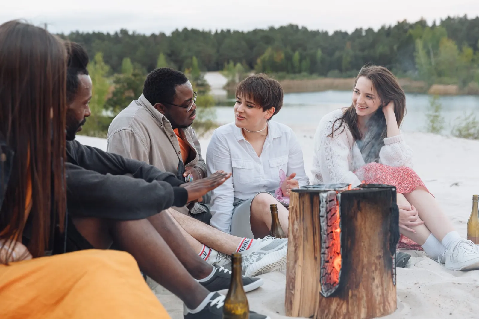 A group of people gathered around a beach fire at dusk