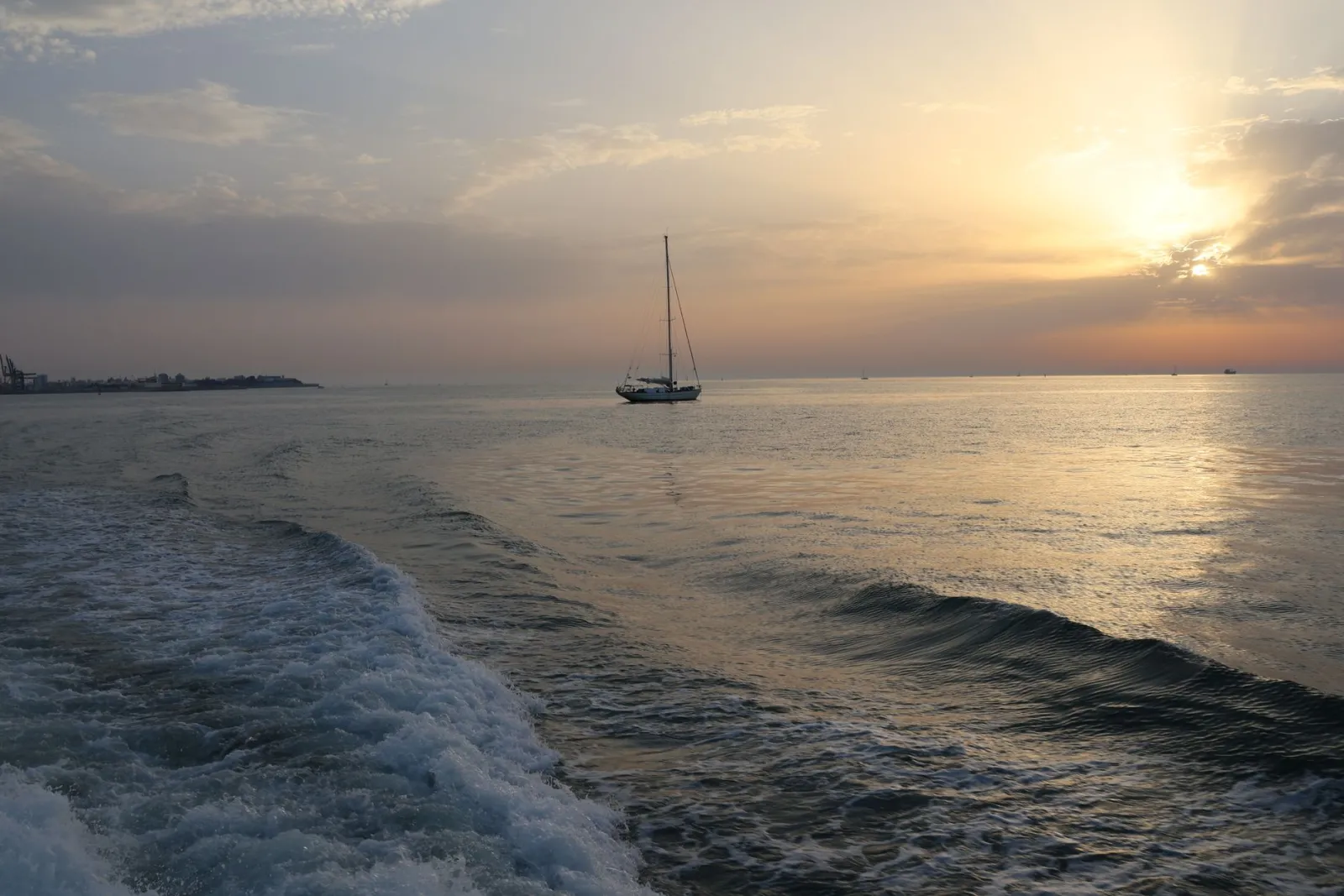 A sailboat gliding across the ocean at sunset