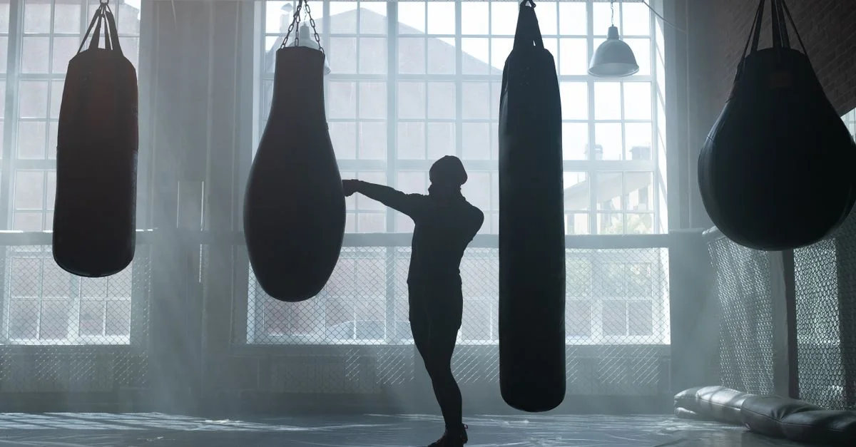 A fighter alone among heavy bags in a smoke-filled gym